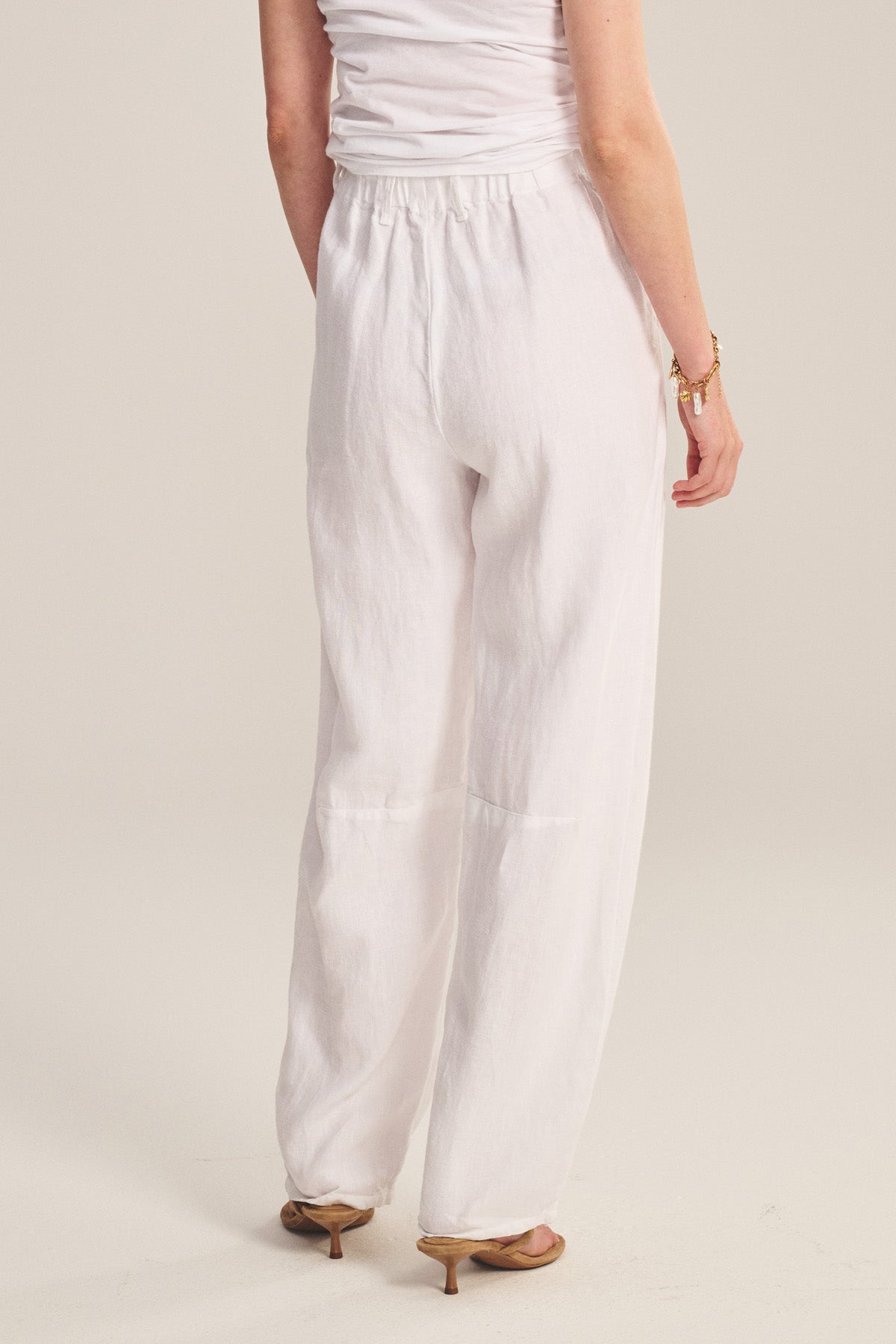 A person is shown from the back wearing TAYLOR HEAVY LINEN PANT by Velvet by Graham & Spencer with a tailored fit, hands in pockets, paired with heeled sandals and a white sleeveless top.-41008421044417