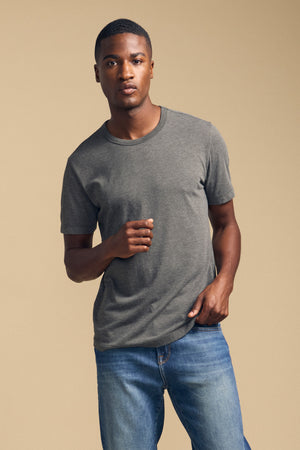 A person wearing the HARRIS TEE by Velvet by Graham & Spencer in a relaxed fit, paired with blue jeans, stands against a plain beige background.