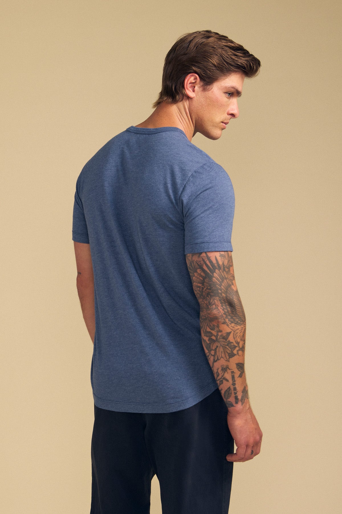 A man wearing the HARRIS TEE by Velvet by Graham & Spencer stands with his back to the camera, displaying a tattooed arm and dark pants against a neutral background.-41702022840513