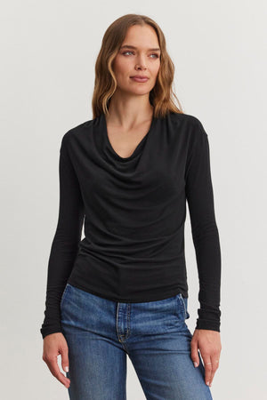 A person with long brown hair is wearing the PATTY TEE in black Tencel™ knit by Velvet by Graham & Spencer, along with blue jeans, standing against a plain white background.