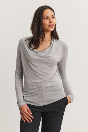 A person wearing a PATTY TEE gray Tencel™ knit cowl neck sweater by Velvet by Graham & Spencer and black pants stands against a plain background.