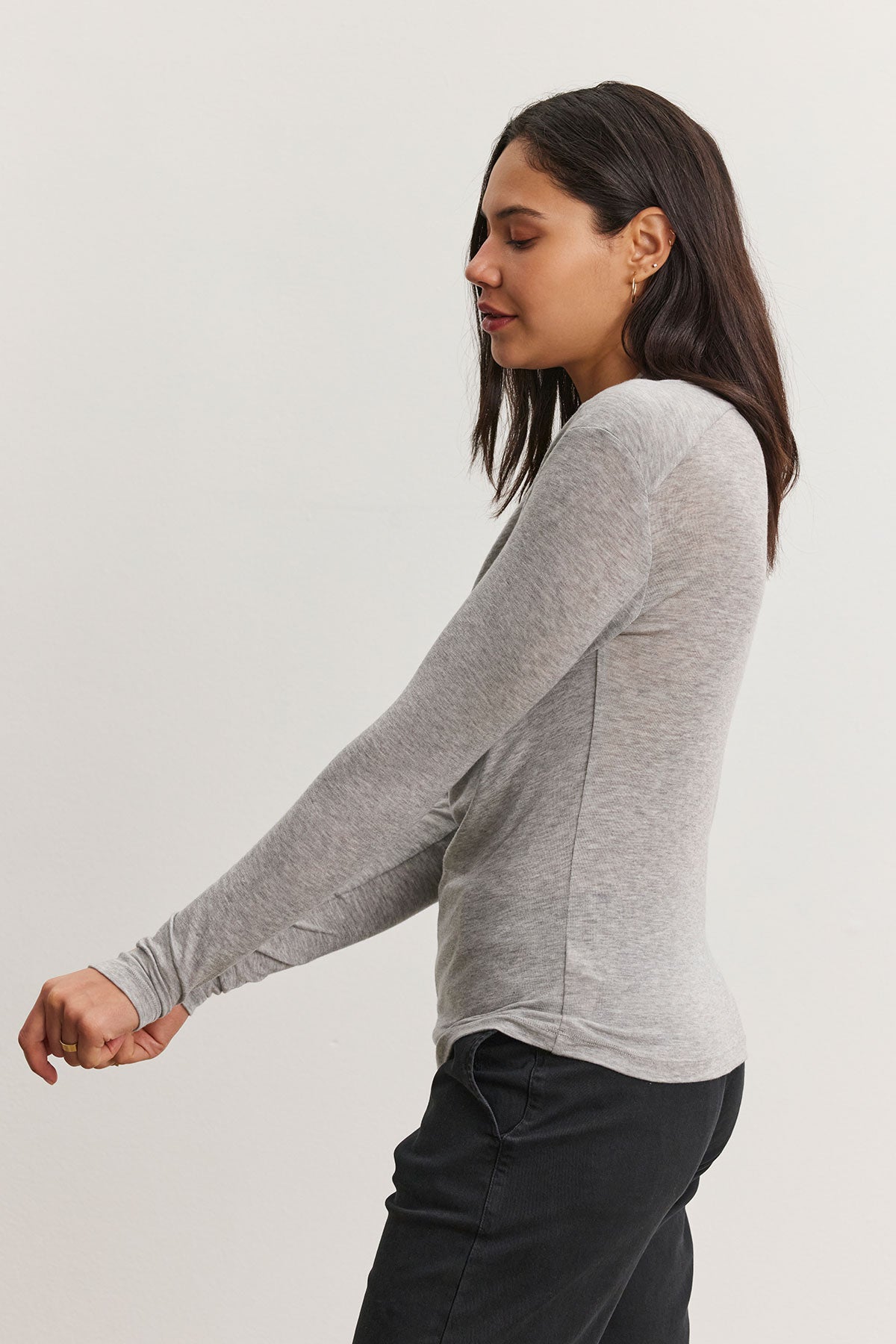   A woman with long dark hair wears the Velvet by Graham & Spencer PATTY TEE and black pants, standing against a neutral background. 