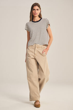 A woman stands against a plain background wearing a short-sleeve striped t-shirt, brown shoes, and the TENLEY PANT by Velvet by Graham & Spencer.
