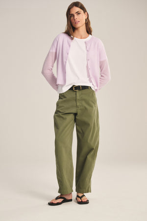 A woman wears the TENLEY PANT by Velvet by Graham & Spencer in a relaxed fit, paired with a light purple cardigan, white t-shirt, black belt, and black sandals against a neutral background.