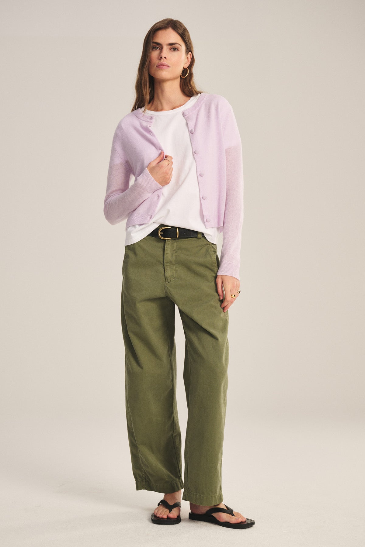 Woman in a studio wears the Velvet by Graham & Spencer TENLEY PANT in olive green, paired with a light purple cardigan, white tee, black belt, black sandals, and gold accessories.-40808733376705