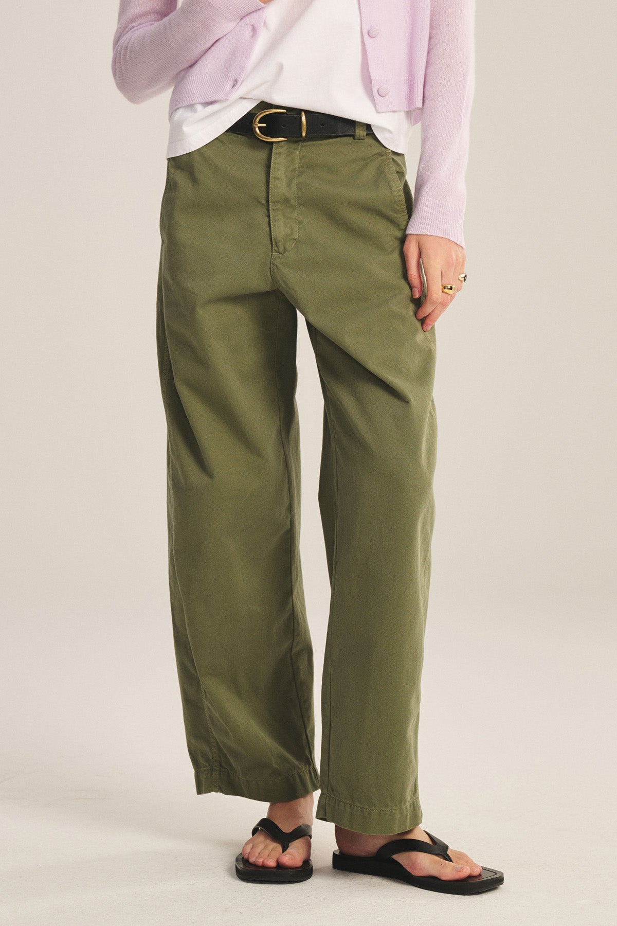 Person wearing the TENLEY PANT by Velvet by Graham & Spencer in olive green cotton twill, styled high-waisted with a relaxed fit, paired with a white tee, pink cardigan, black belt, and black sandals against a neutral background.-40808733343937