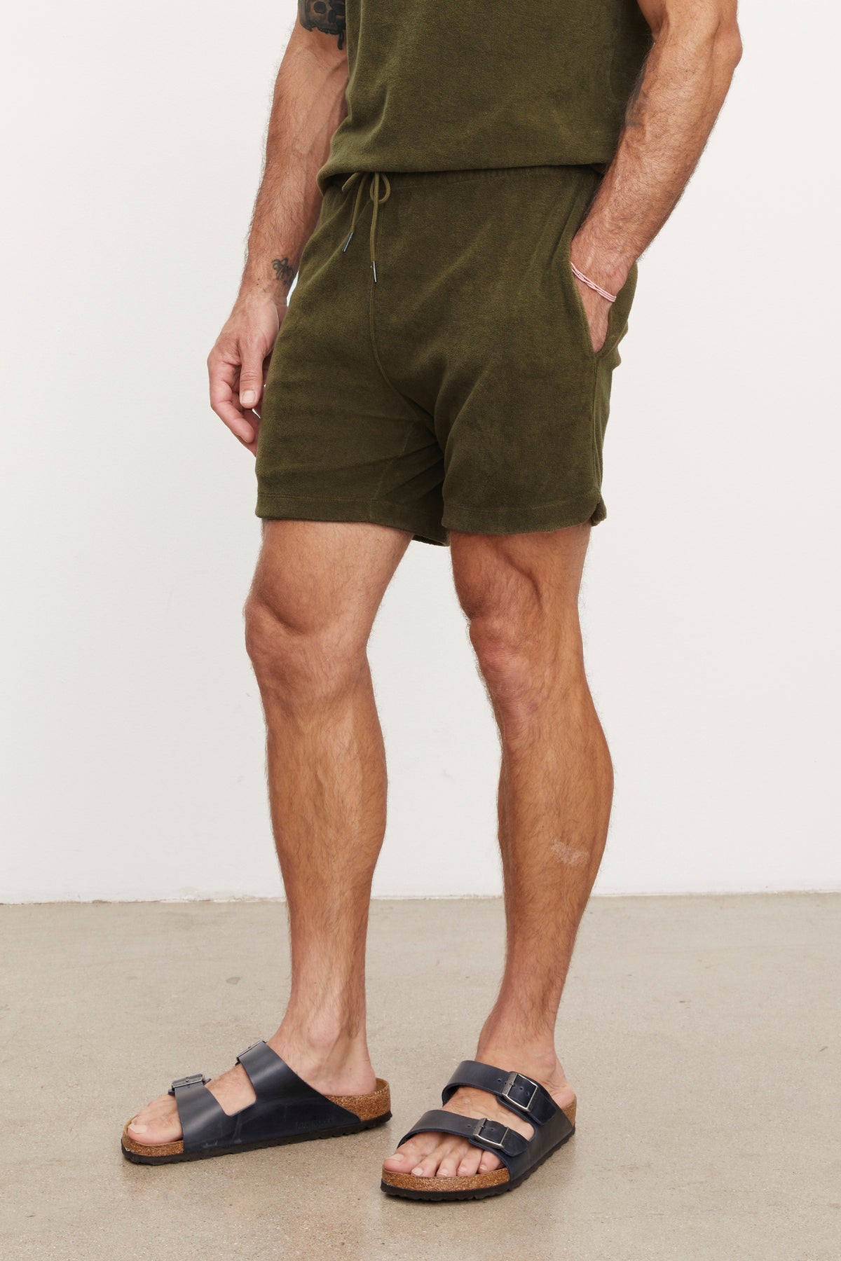 Man standing in a studio wearing green Velvet by Graham & Spencer Salem shorts and black sandals, focusing on his lower half.-36753587699905