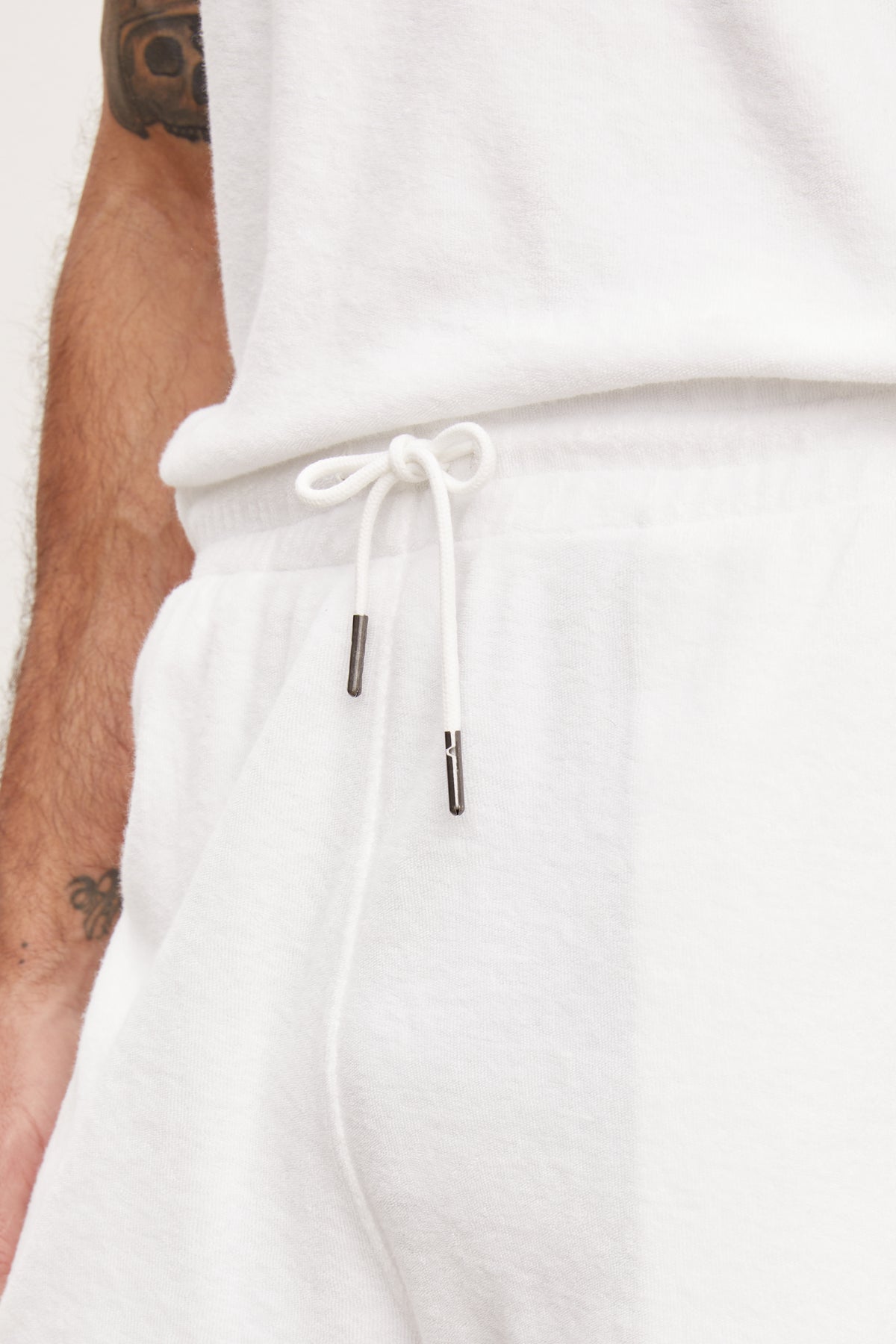 Close-up of a white drawstring with metal aglets on Velvet by Graham & Spencer's SALEM SHORT lounging shorts, against a man's side with a visible arm tattoo.-36943667921089