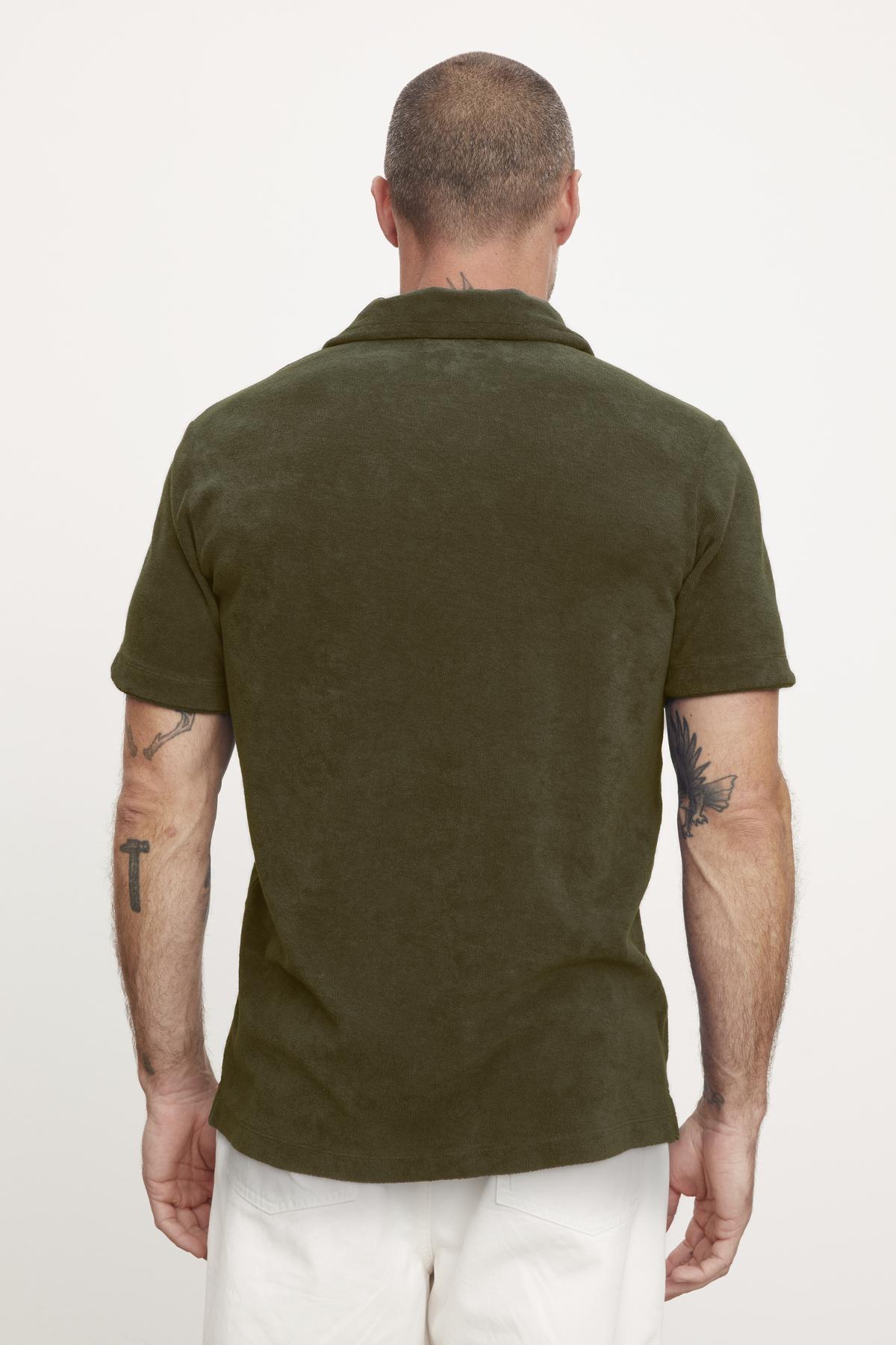 Rear view of a man in a Velvet by Graham & Spencer Sergey polo shirt and white pants, showing a tattoo on his left arm.-36890717913281