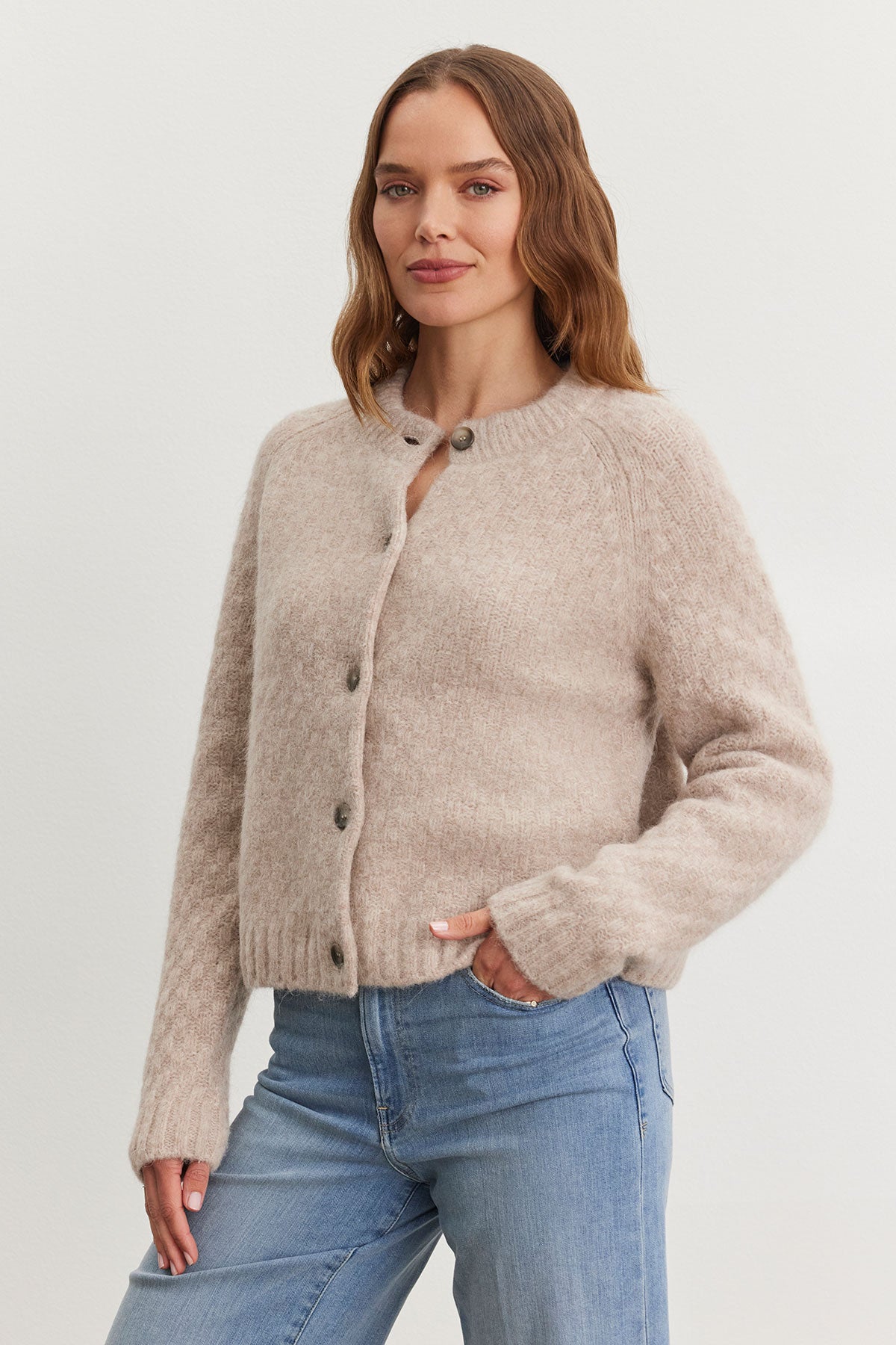 A person stands wearing the CHANTAL ALPACA CARDIGAN by Velvet by Graham & Spencer, layered over a textured sweater and paired with blue jeans against a plain background.-38301315498177