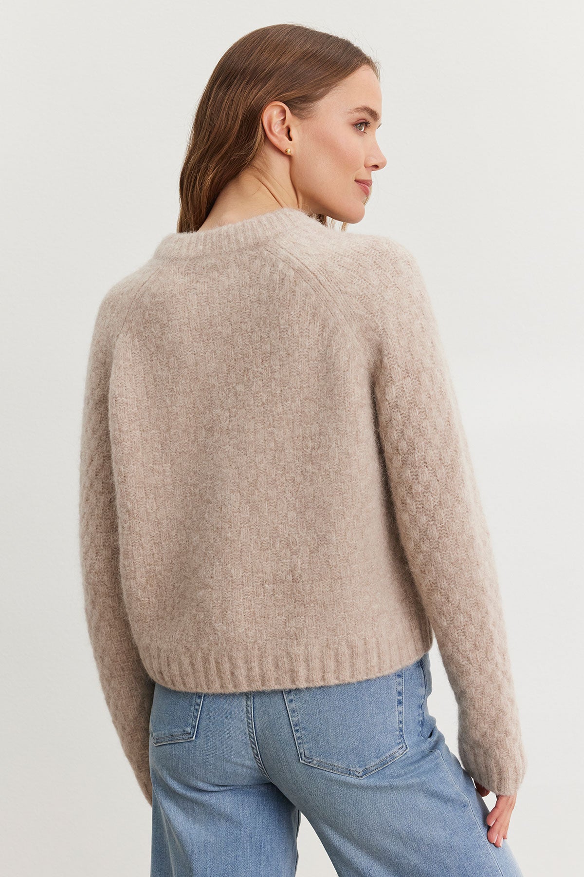   A person wearing the Velvet by Graham & Spencer's CHANTAL ALPACA CARDIGAN, featuring ribbed trims, paired with blue jeans is turned sideways, facing left. 