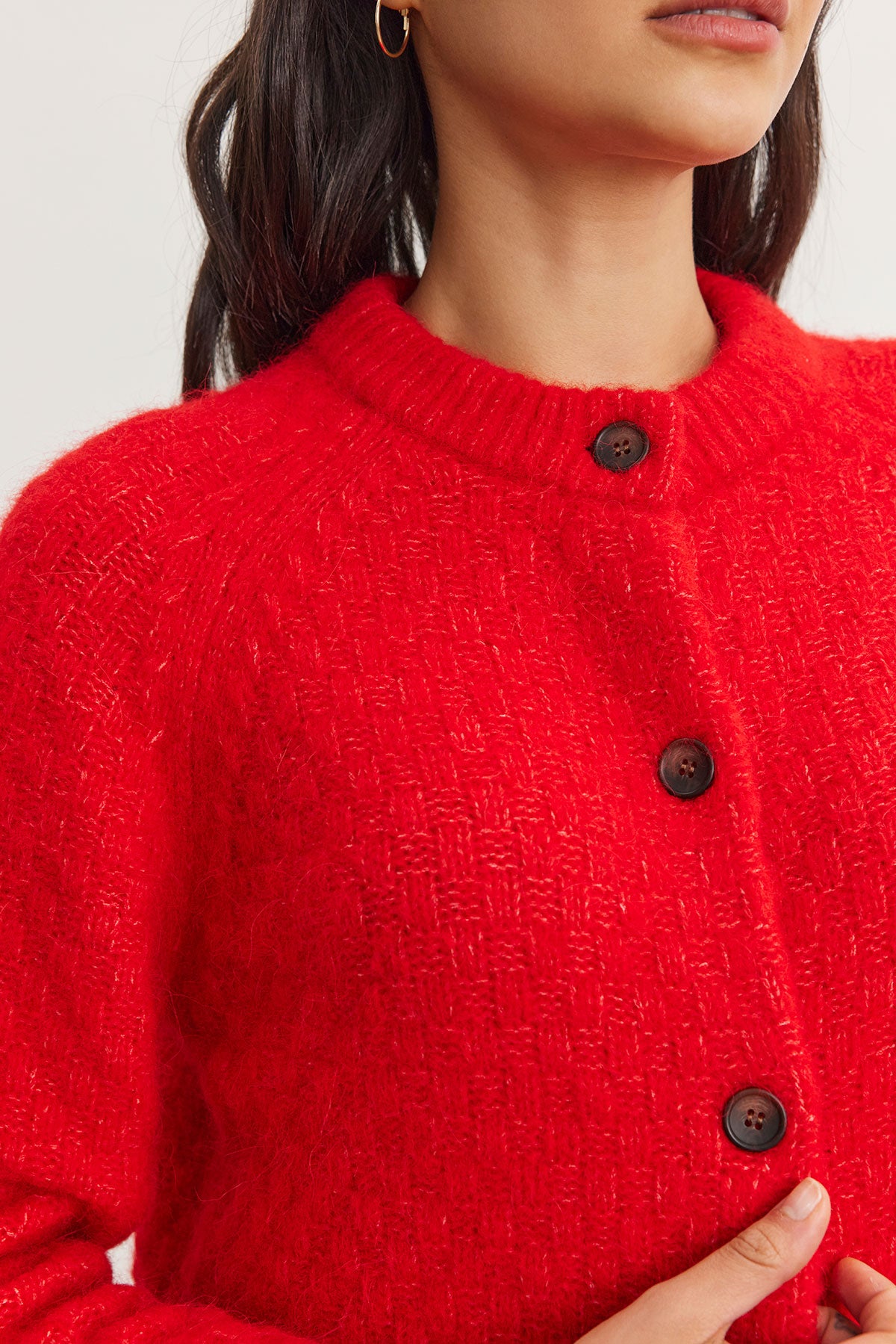   A person wearing the CHANTAL ALPACA CARDIGAN by Velvet by Graham & Spencer, crafted from a vibrant red alpaca blend and embellished with large buttons. 