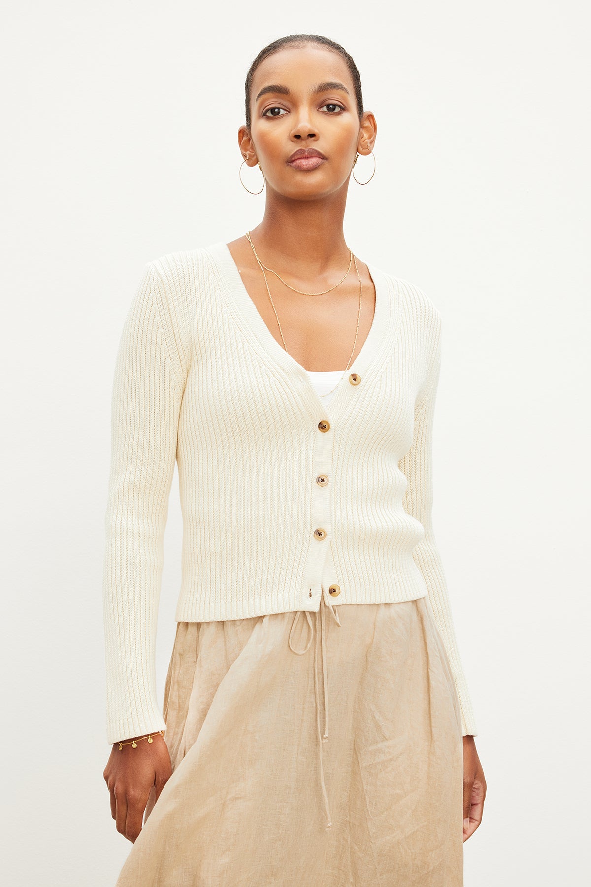 The model is showcasing a versatile choice by wearing a HYDIE BUTTON FRONT CARDIGAN from Velvet by Graham & Spencer and a tan skirt, perfect for all seasons.-35967413747905