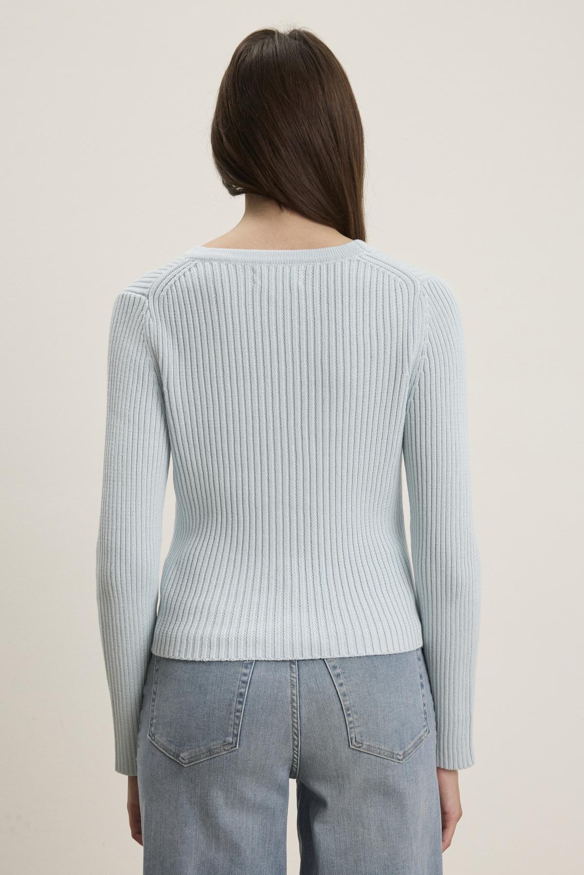   A person with long hair is wearing the HYDIE CARDIGAN in light blue by Velvet by Graham & Spencer and blue jeans, facing away. 