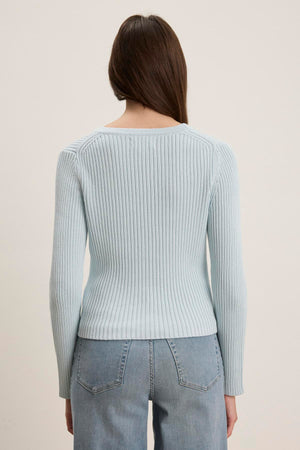 A person with long hair is wearing the HYDIE CARDIGAN in light blue by Velvet by Graham & Spencer and blue jeans, facing away.