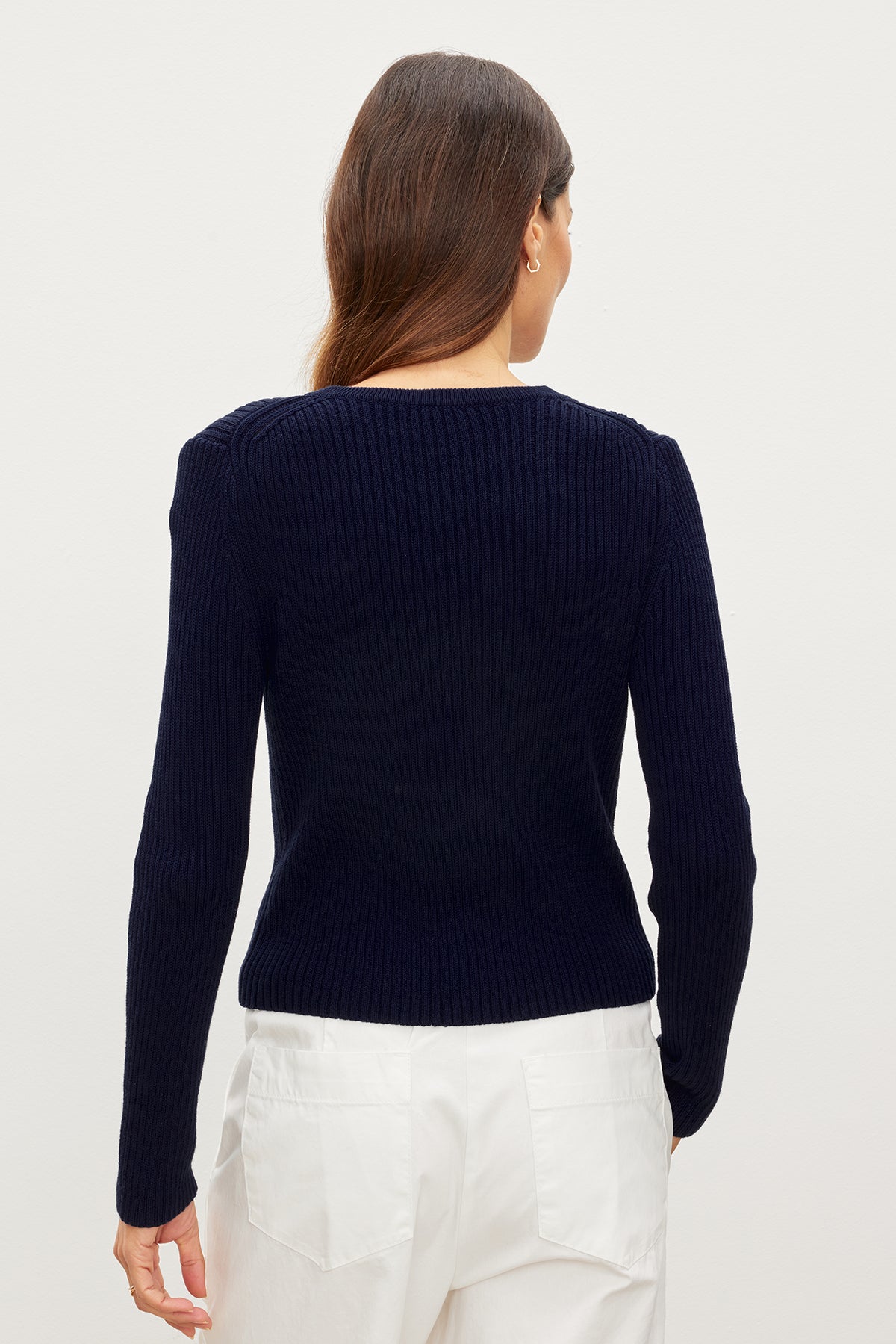  The back view of a woman wearing a Velvet by Graham & Spencer HYDIE BUTTON FRONT CARDIGAN and white pants. 