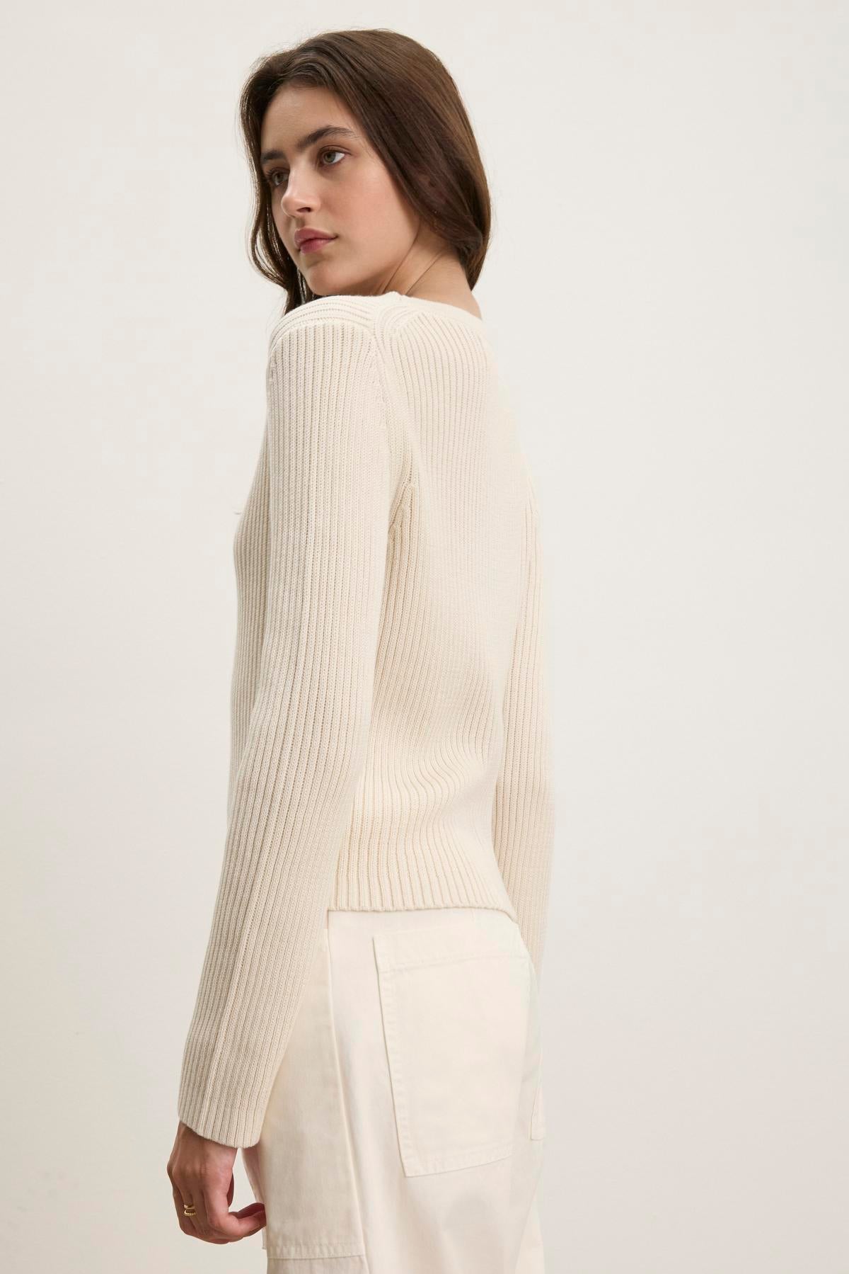   A person wearing the HYDIE CARDIGAN by Velvet by Graham & Spencer and light pants stands looking over their shoulder against a plain background. 