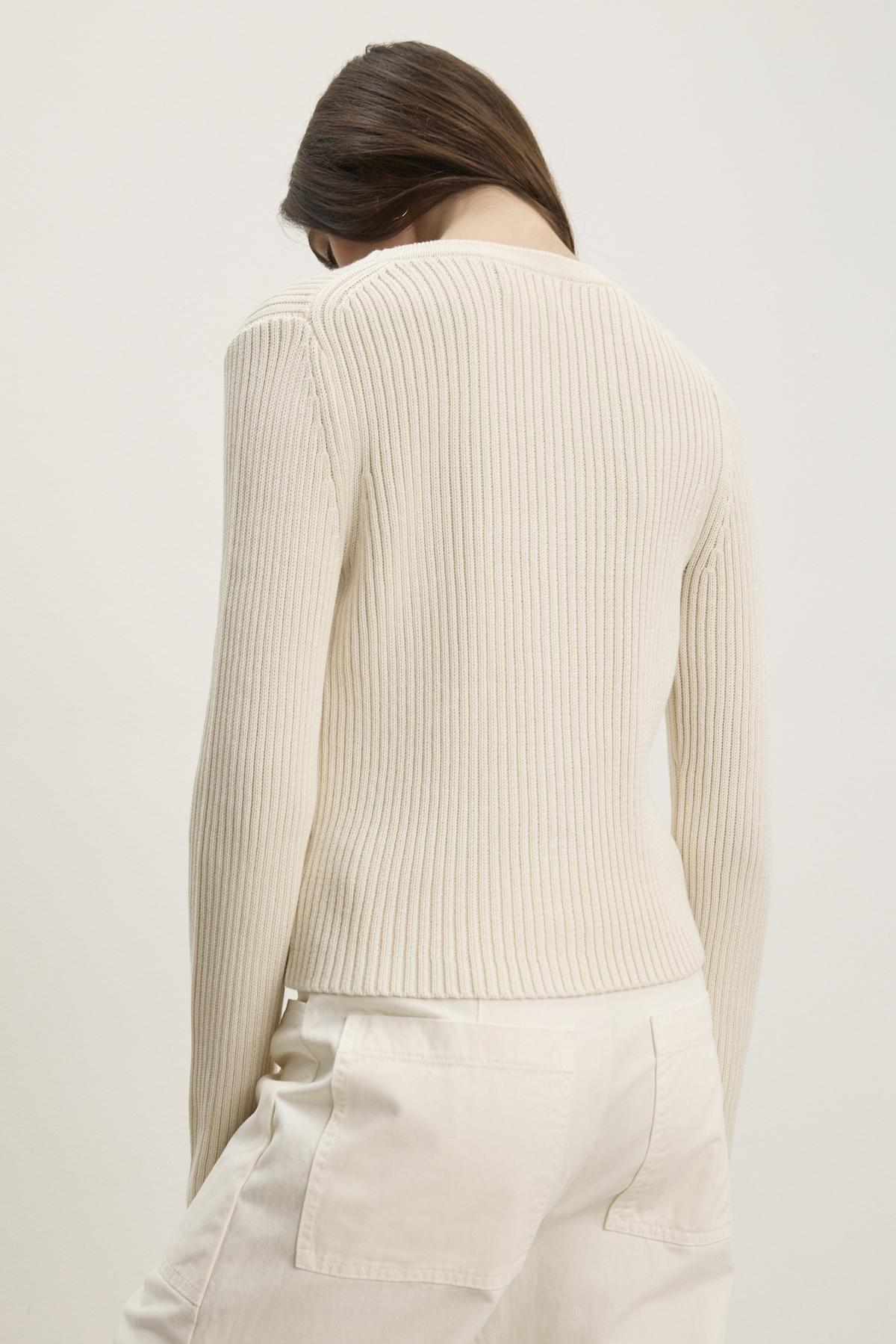   A person wearing a HYDIE CARDIGAN from Velvet by Graham & Spencer, paired with white pants, facing away. 