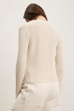 A person wearing a HYDIE CARDIGAN from Velvet by Graham & Spencer, paired with white pants, facing away.