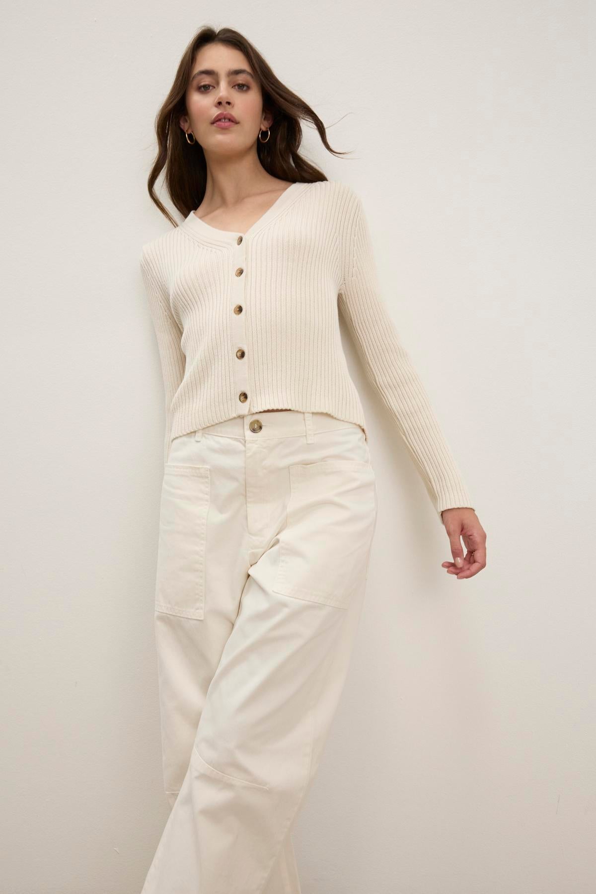   A woman wears the HYDIE CARDIGAN by Velvet by Graham & Spencer with cream pants, standing against a plain background. 