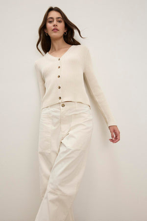 A woman wears the HYDIE CARDIGAN by Velvet by Graham & Spencer with cream pants, standing against a plain background.