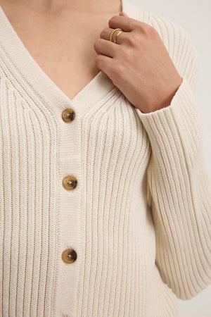 Close-up of a person wearing the HYDIE CARDIGAN by Velvet by Graham & Spencer, featuring wooden buttons, with gold rings on their hand.