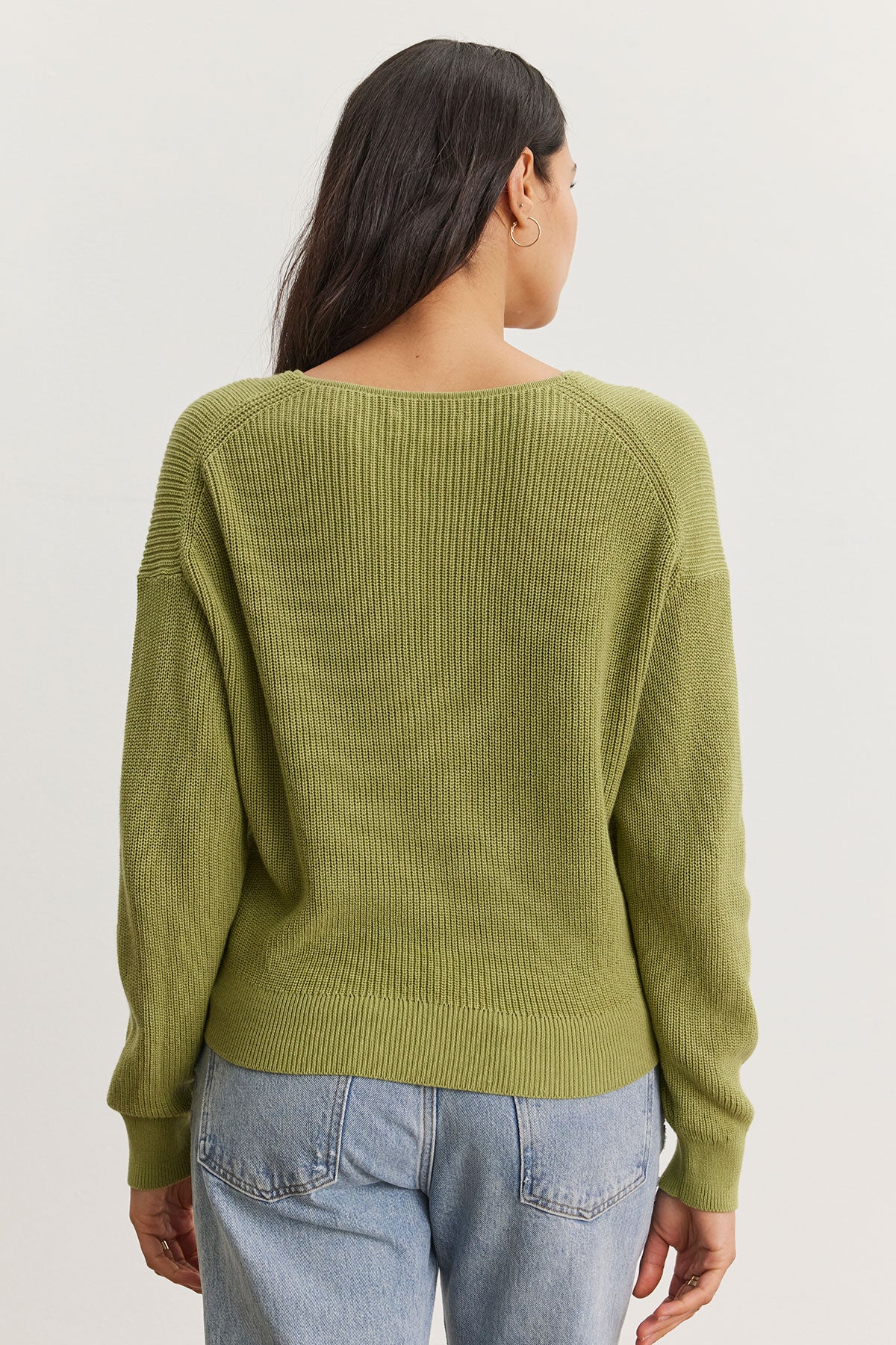   Woman viewed from behind wearing a Velvet by Graham & Spencer Tava Cardigan and faded blue jeans, standing against a plain white background. 