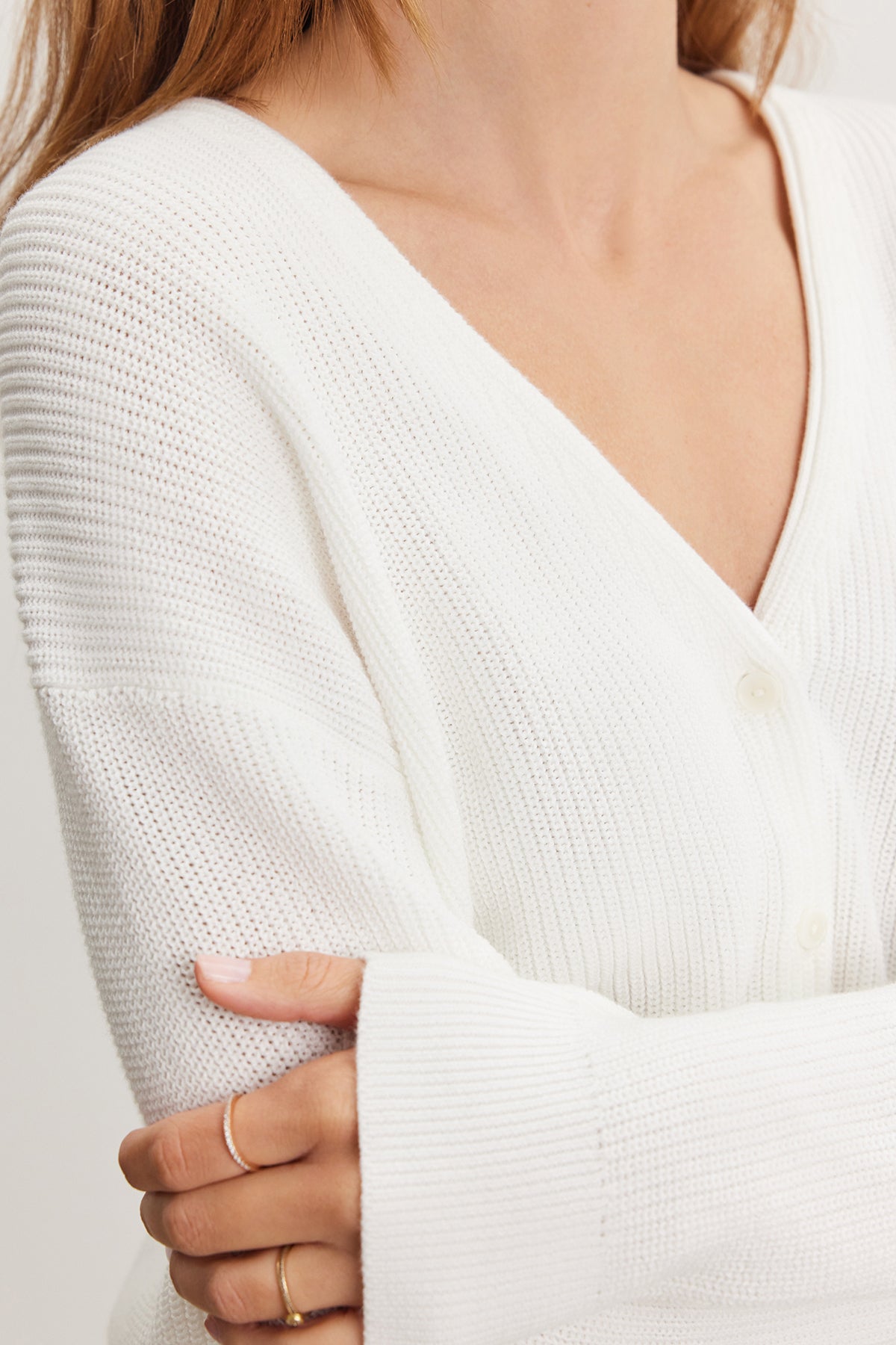   Close-up of a woman in a Velvet by Graham & Spencer Tava cardigan, focusing on the textured cotton knit fabric and her crossed arms with a visible gold ring on her finger. 