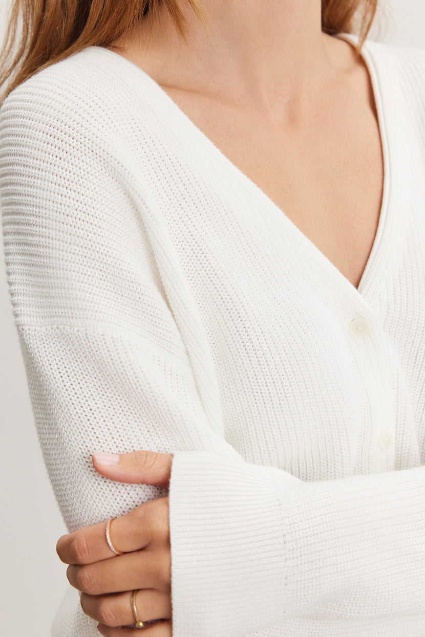 Close-up of a woman in a Velvet by Graham & Spencer Tava cardigan, focusing on the textured cotton knit fabric and her crossed arms with a visible gold ring on her finger.