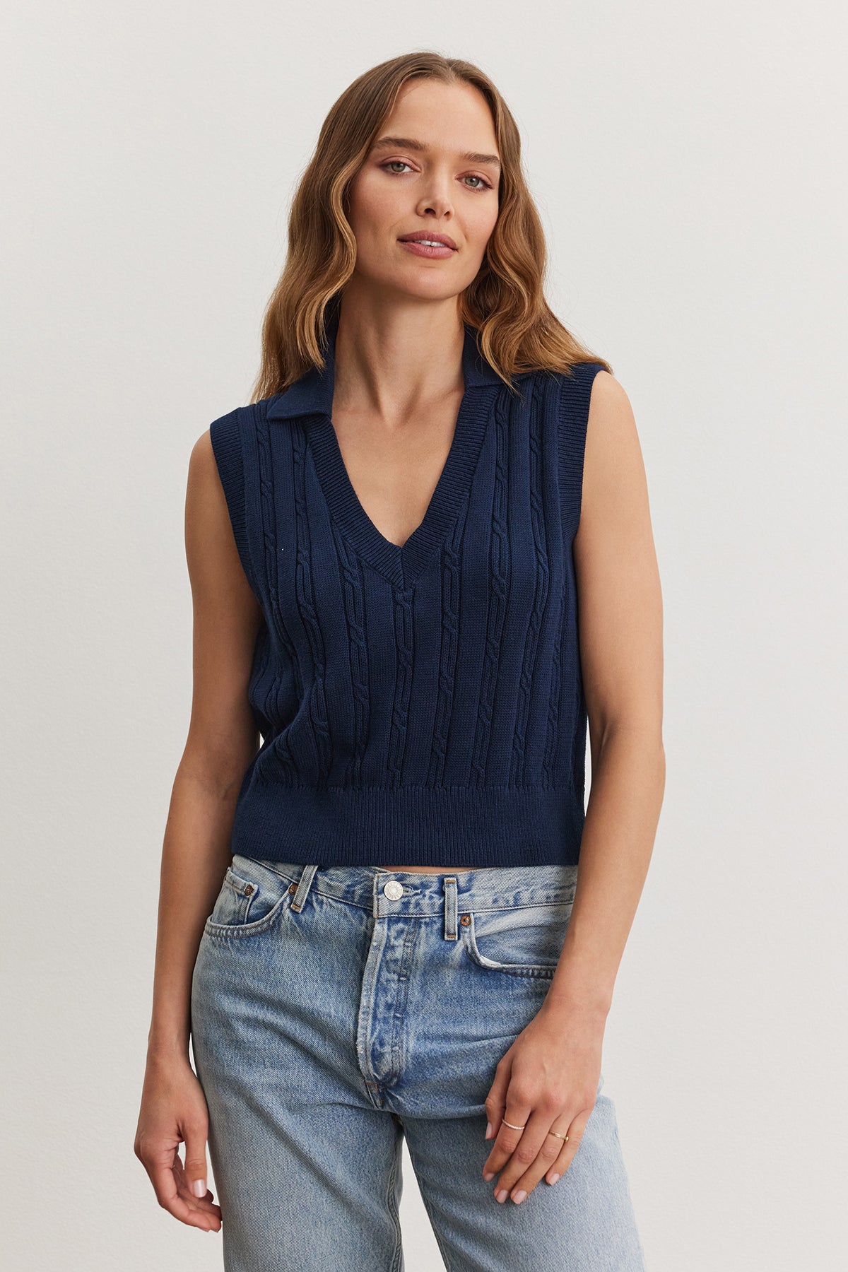 A woman wearing a navy blue WENDY SWEATER VEST and light blue jeans stands against a neutral background. Brand: Velvet by Graham & Spencer-36909568458945