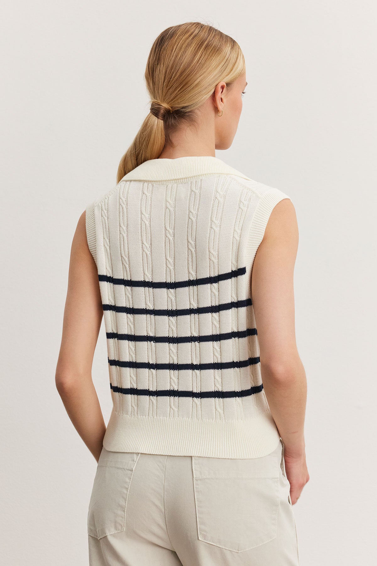   Woman viewed from behind, wearing a white Velvet by Graham & Spencer WENDY SWEATER VEST with horizontal black stripes, paired with beige pants. 