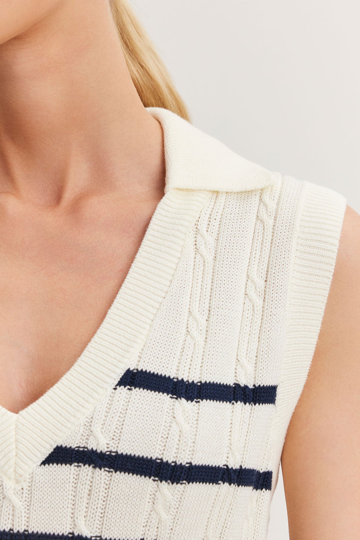   Close-up of a woman wearing a Velvet by Graham & Spencer WENDY SWEATER VEST in cream-colored cable knit with a navy blue stripe detail. 