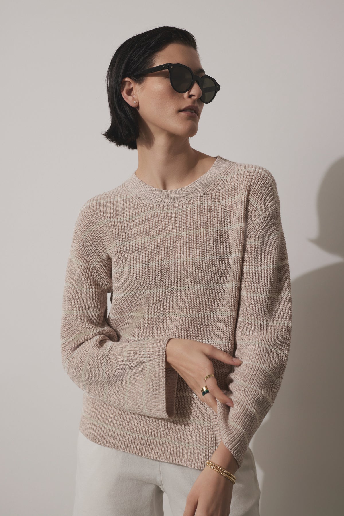 A stylish woman wearing a Velvet by Jenny Graham INDIO LINEN SWEATER and sunglasses poses with one hand on her hip against a light background.-36863294963905