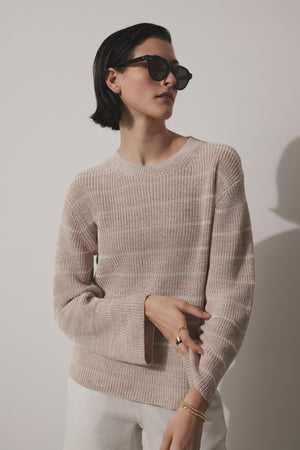 A stylish woman wearing a Velvet by Jenny Graham INDIO LINEN SWEATER and sunglasses poses with one hand on her hip against a light background.