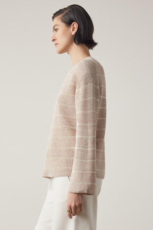 Side profile of a person with short dark hair wearing a beige textured Indio Linen Sweater from Velvet by Jenny Graham and white pants against a light background.