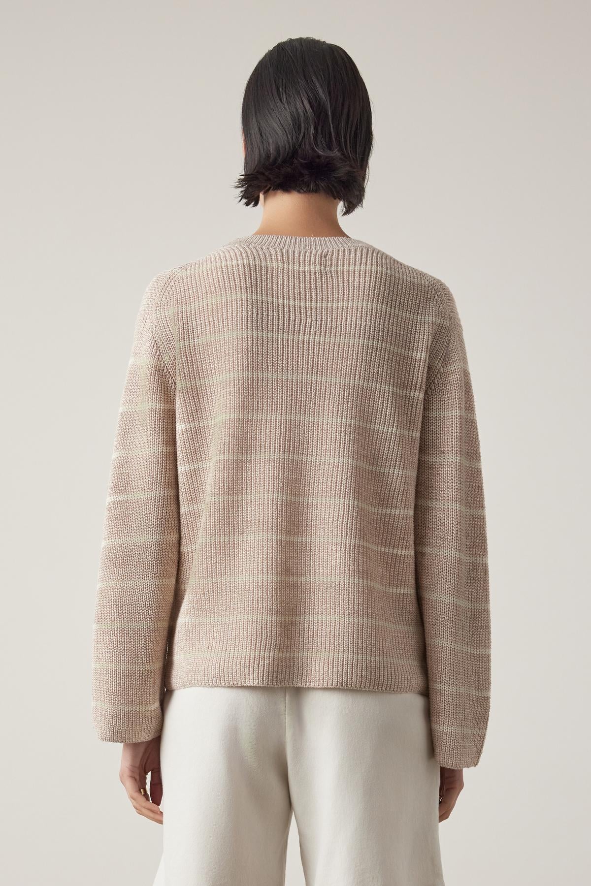 Rear view of a person with short dark hair wearing a beige ribbed Indio Linen Sweater by Velvet by Jenny Graham and white pants against a light beige background.-36863295029441