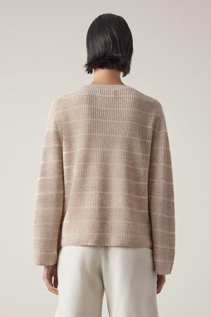 Rear view of a person with short dark hair wearing a beige ribbed Indio Linen Sweater by Velvet by Jenny Graham and white pants against a light beige background.