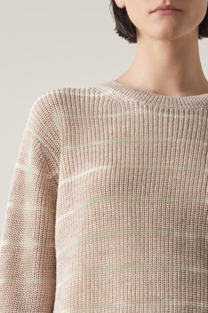 Close-up of a woman wearing a sheer, Velvet by Jenny Graham INDIO LINEN SWEATER in neutral stripes, focusing on the sweater's texture and pattern.
