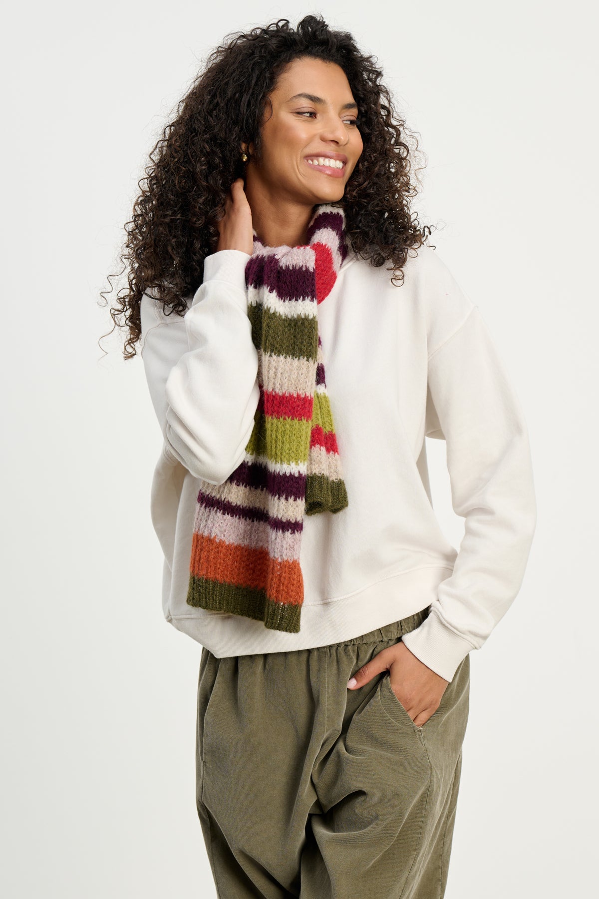 A person in a white sweatshirt and olive green pants showcases the LUCA ALPACA SCARF by Velvet by Graham & Spencer—a cozy, colorful accessory that brings warmth and style against a plain background.-39742257823937