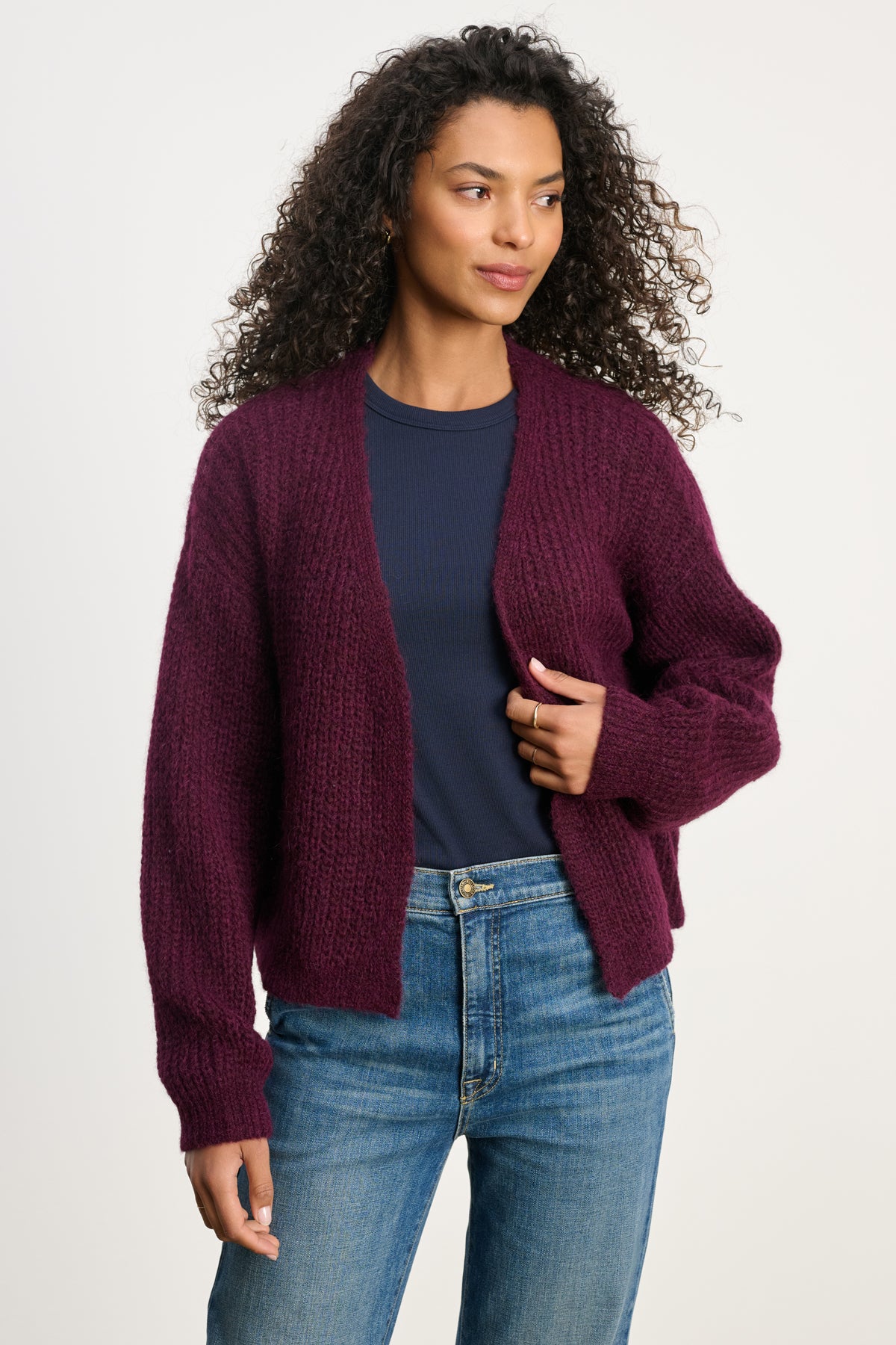A woman wears the RANYA ALPACA CARDIGAN by Velvet by Graham & Spencer over a navy blue t-shirt and blue jeans, standing against a plain light background.-40227142664385