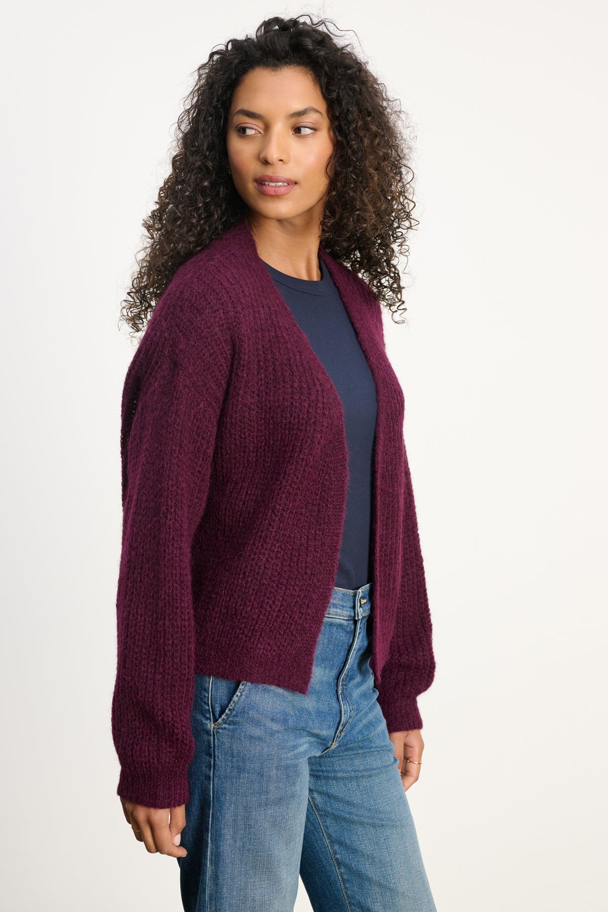 A woman wears the RANYA ALPACA CARDIGAN by Velvet by Graham & Spencer—a dark purple wrap-style alpaca blend—over a navy top and blue jeans, standing against a plain white background.-40227142697153