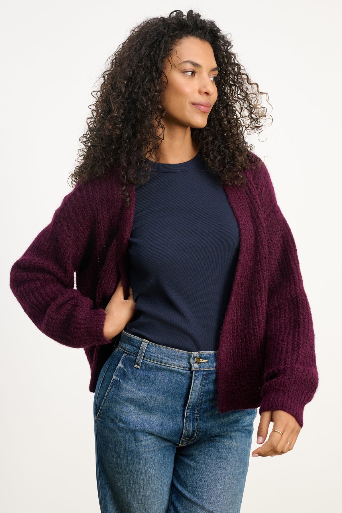 A person in a dark blue t-shirt, blue jeans, and the RANYA ALPACA CARDIGAN by Velvet by Graham & Spencer stands against a plain light background—a perfect look for cozy layering.
