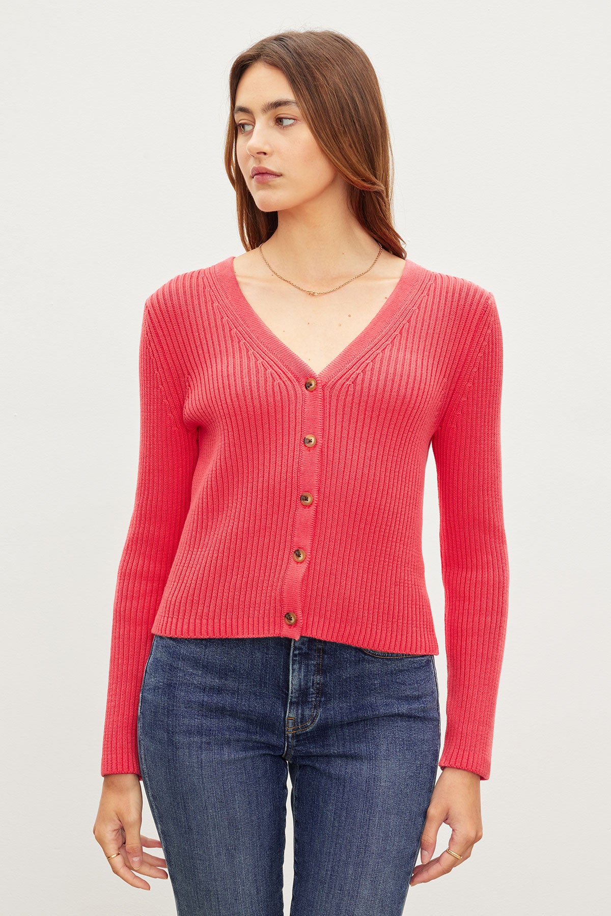 Woman in a red cotton ribbed knit HYDIE BUTTON FRONT CARDIGAN by Velvet by Graham & Spencer and blue jeans standing against a light background.-36387940368577