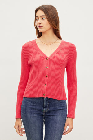 Woman in a red cotton ribbed knit HYDIE BUTTON FRONT CARDIGAN by Velvet by Graham & Spencer and blue jeans standing against a light background.