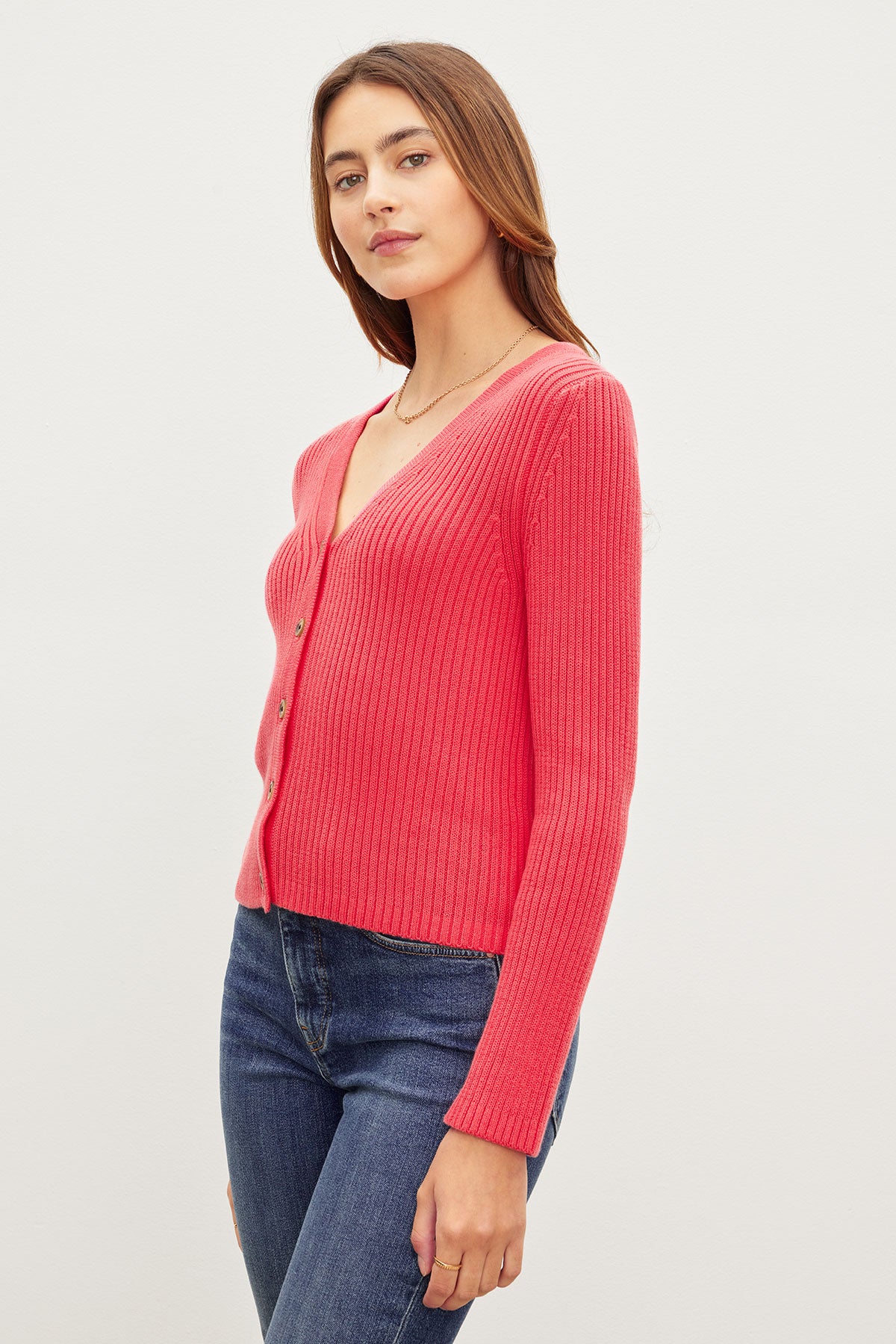   A woman in a red Velvet by Graham & Spencer HYDIE BUTTON FRONT CARDIGAN and blue jeans standing against a plain background, looking at the camera. 