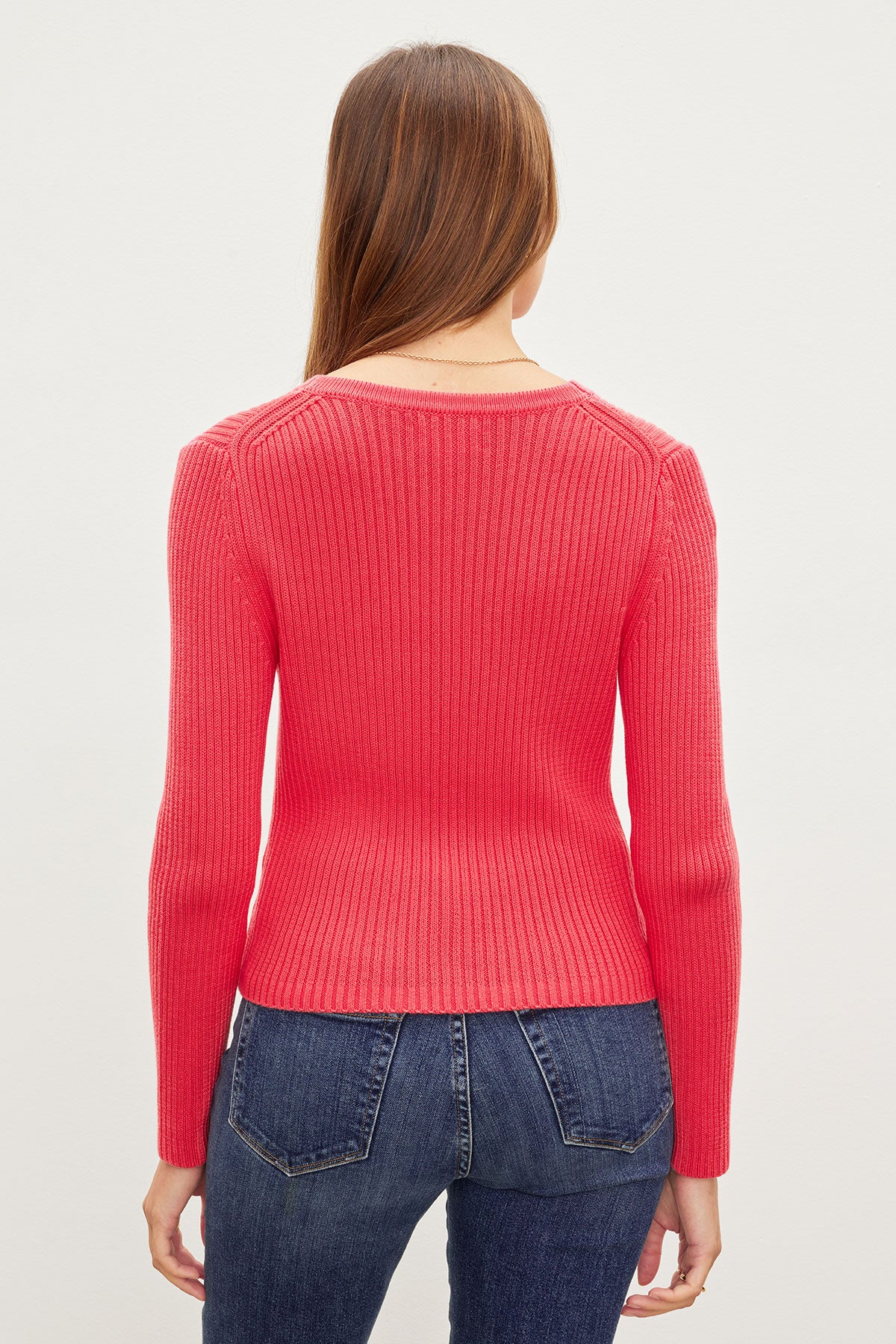 Woman standing with her back to the camera, wearing a red cotton ribbed knit HYDIE BUTTON FRONT CARDIGAN by Velvet by Graham & Spencer and blue jeans against a plain background.-36387940434113