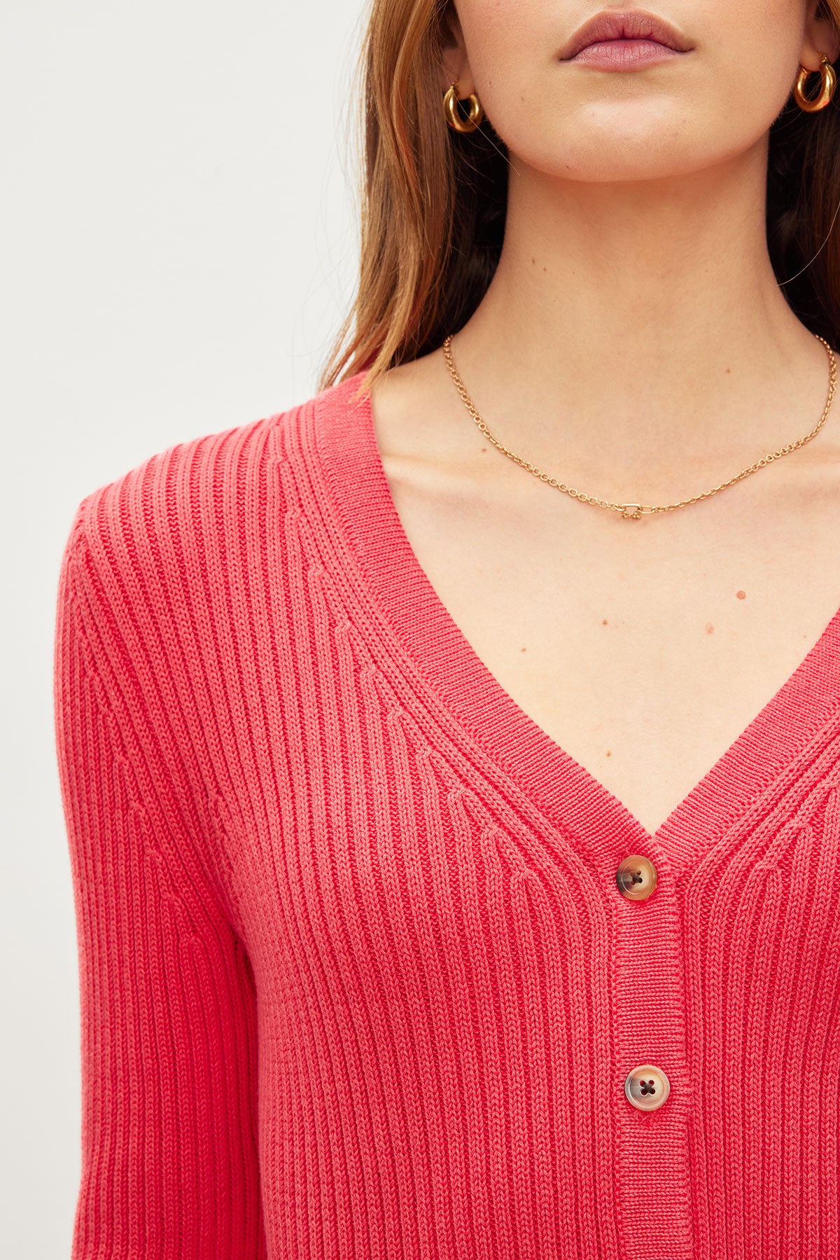   Close-up of a woman wearing a Velvet by Graham & Spencer HYDIE BUTTON FRONT CARDIGAN in coral cotton ribbed knit with buttons, a subtle necklace, and hoop earrings. 