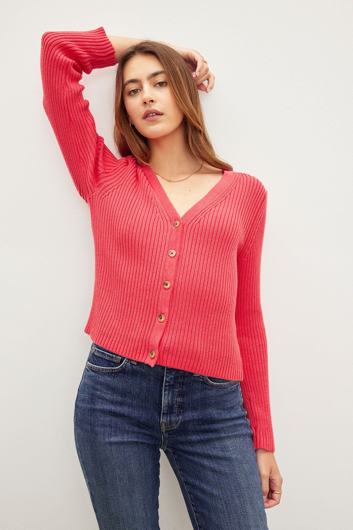 A young woman in a red HYDIE BUTTON FRONT CARDIGAN and blue jeans posing against a white background by Velvet by Graham & Spencer.-36387940499649