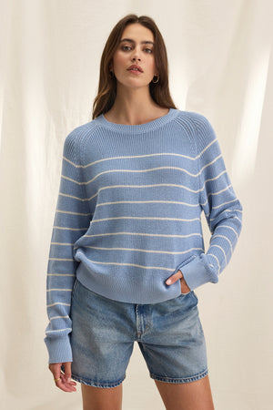 Wearing the Velvet by Graham & Spencer CHAYSE SWEATER with denim shorts epitomizes casual wear, standing out effortlessly against a light, textured background.