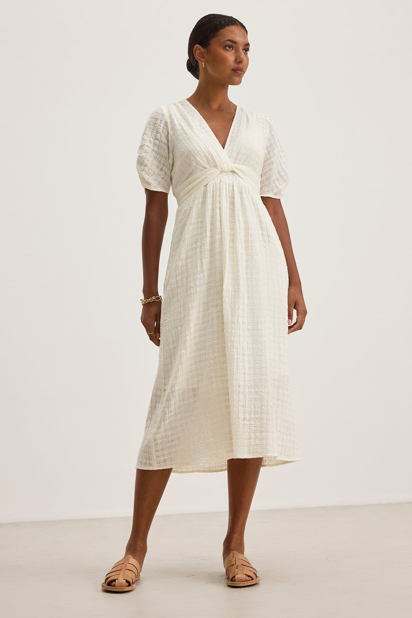 Someone is wearing Velvet by Graham & Spencer's Eloise Textured Cotton Gauze Dress, a white midi dress with a V-neckline and short sleeves, paired with beige sandals on a plain background.